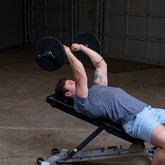 Man performing a bench press exercise with black standard plates, focusing on strength training and muscle building.